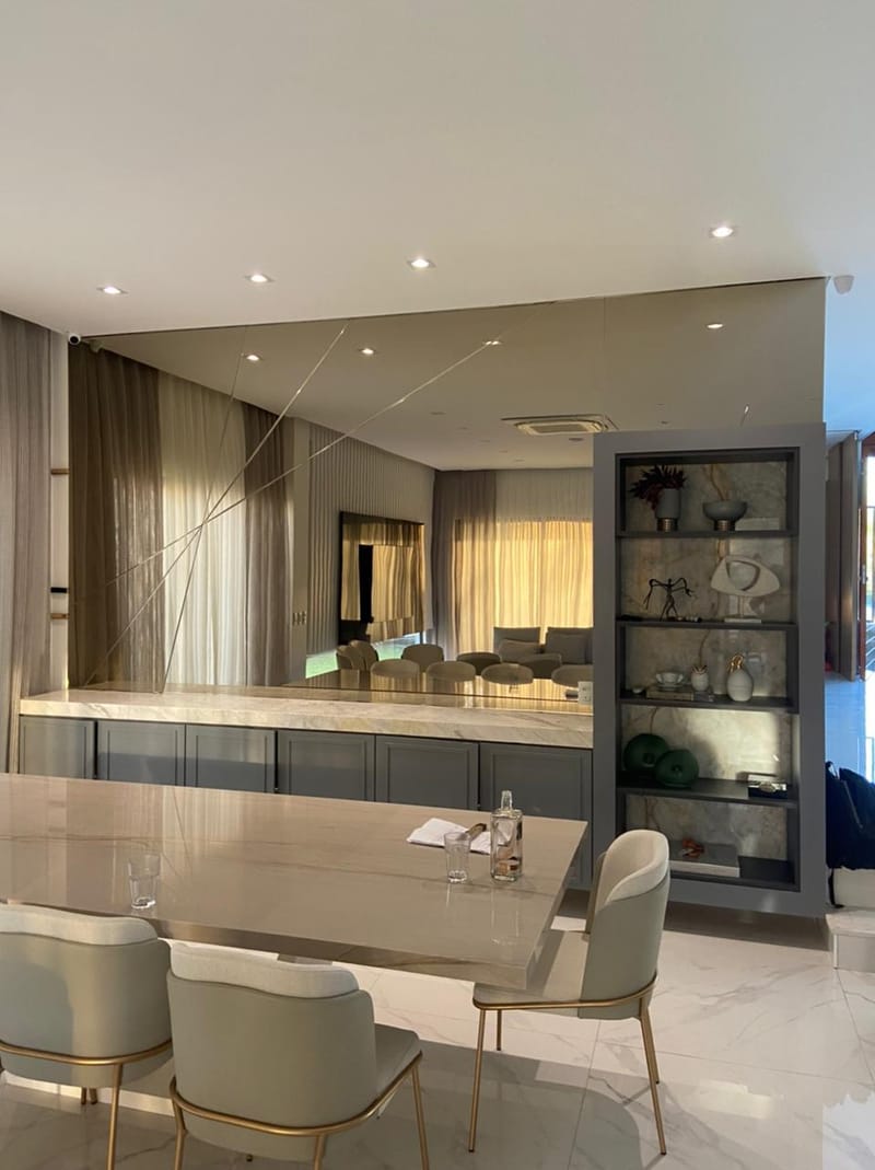Painel de espelho de parede inteira refletindo sala de jantar e estar, com estante de mármore ao lado